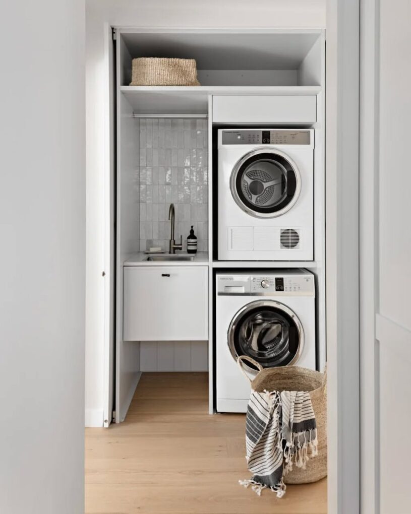 Bright apartment laundry room featuring light wood acoustic slatted wall paneling and modern white appliances