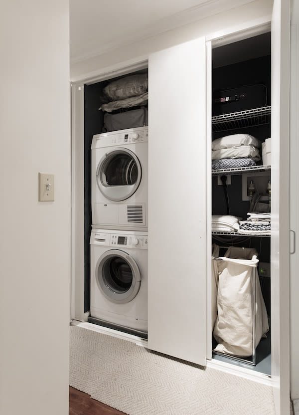 Bright white apartment laundry space with woven rattan cabinet fronts, light ash wood counters, and bright illumination.