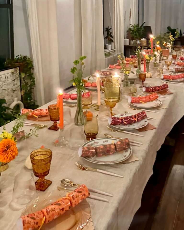 Long banquet table set with colorful party crackers, decorative trays, gold flatware, soft ambient lighting