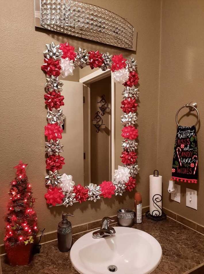 Bathroom vanity mirror framed by a red satin bow, a petite tabletop fir tree, and soft ivory towels.