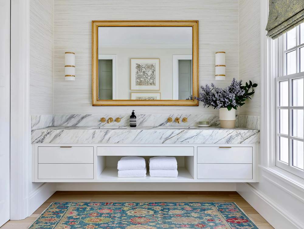 Vertical stacked cream subway tile wall warm oak vanity brass hardware soft pendant light glowing overhead.