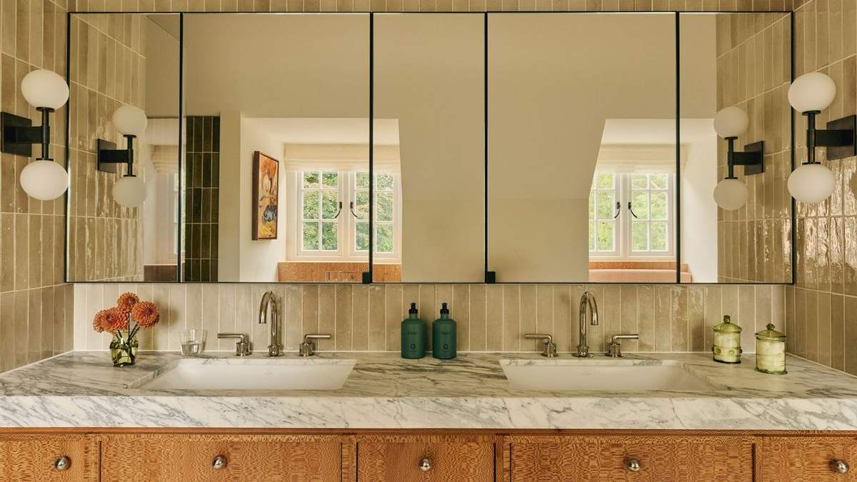 Trendy bathroom with a hexagon mirror, patterned floor tiles, and gold wall sconces.