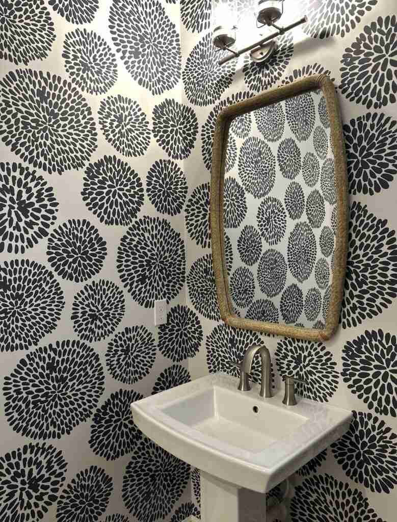 Compact powder room featuring black white floral wallpaper white pedestal sink sleek sconce lighting.