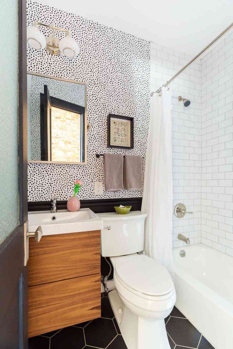 Modern bathroom with geometric black white wallpaper white porcelain tub warm pendant light sconce.