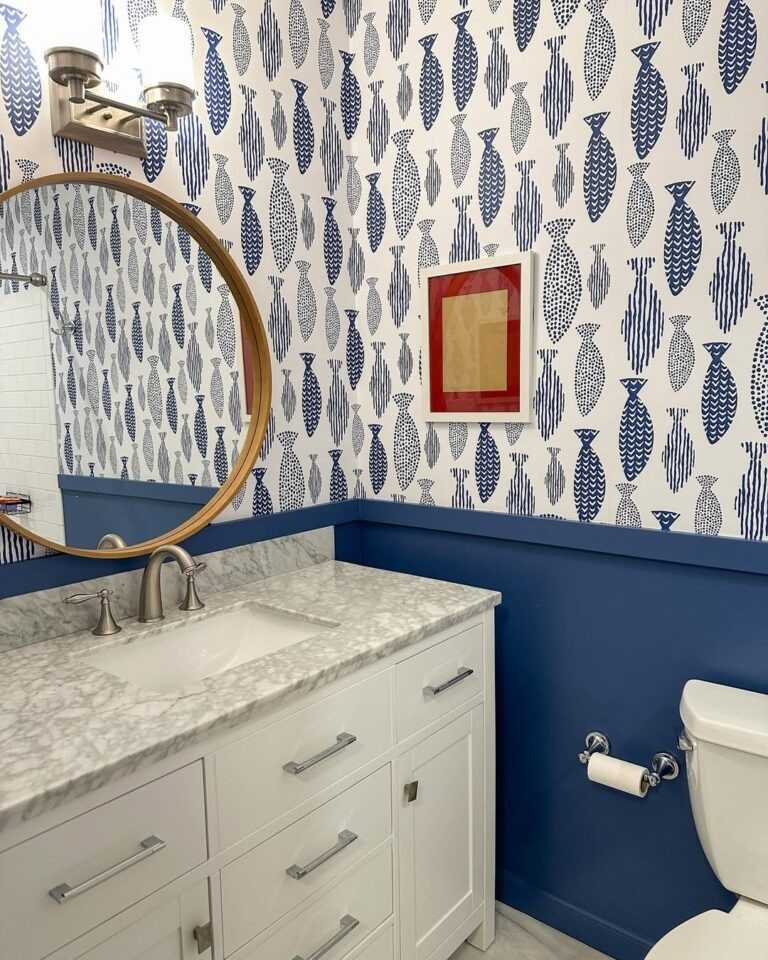 Coastal bathroom featuring blue fish pattern wallpaper white vanity unit polished chrome lighting fixtures.