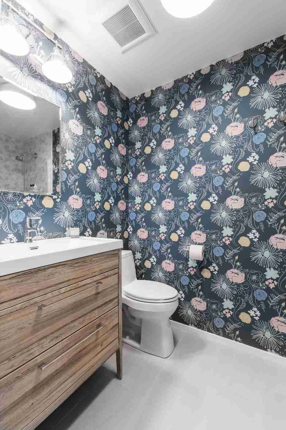 English country bathroom with blue floral wallpaper white vanity table warm brass sconce lighting.