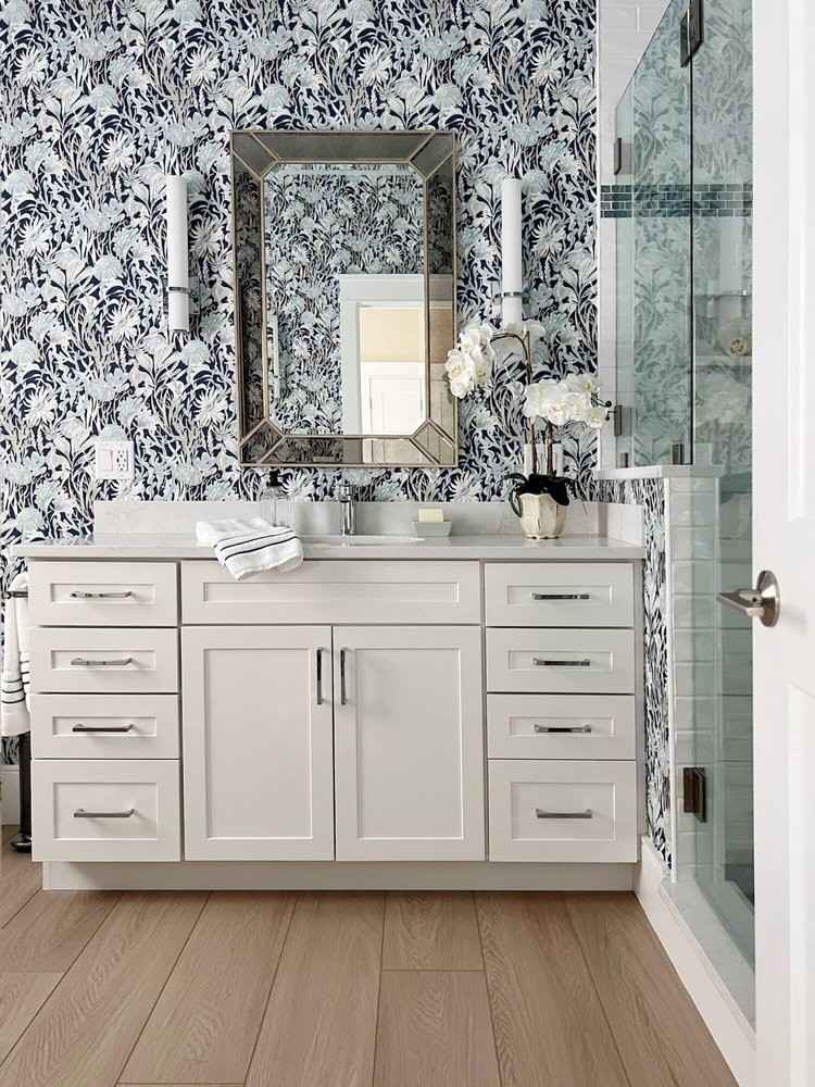 Bright powder room with soft blue floral wallpaper white marble vanity warm brass mirror light.