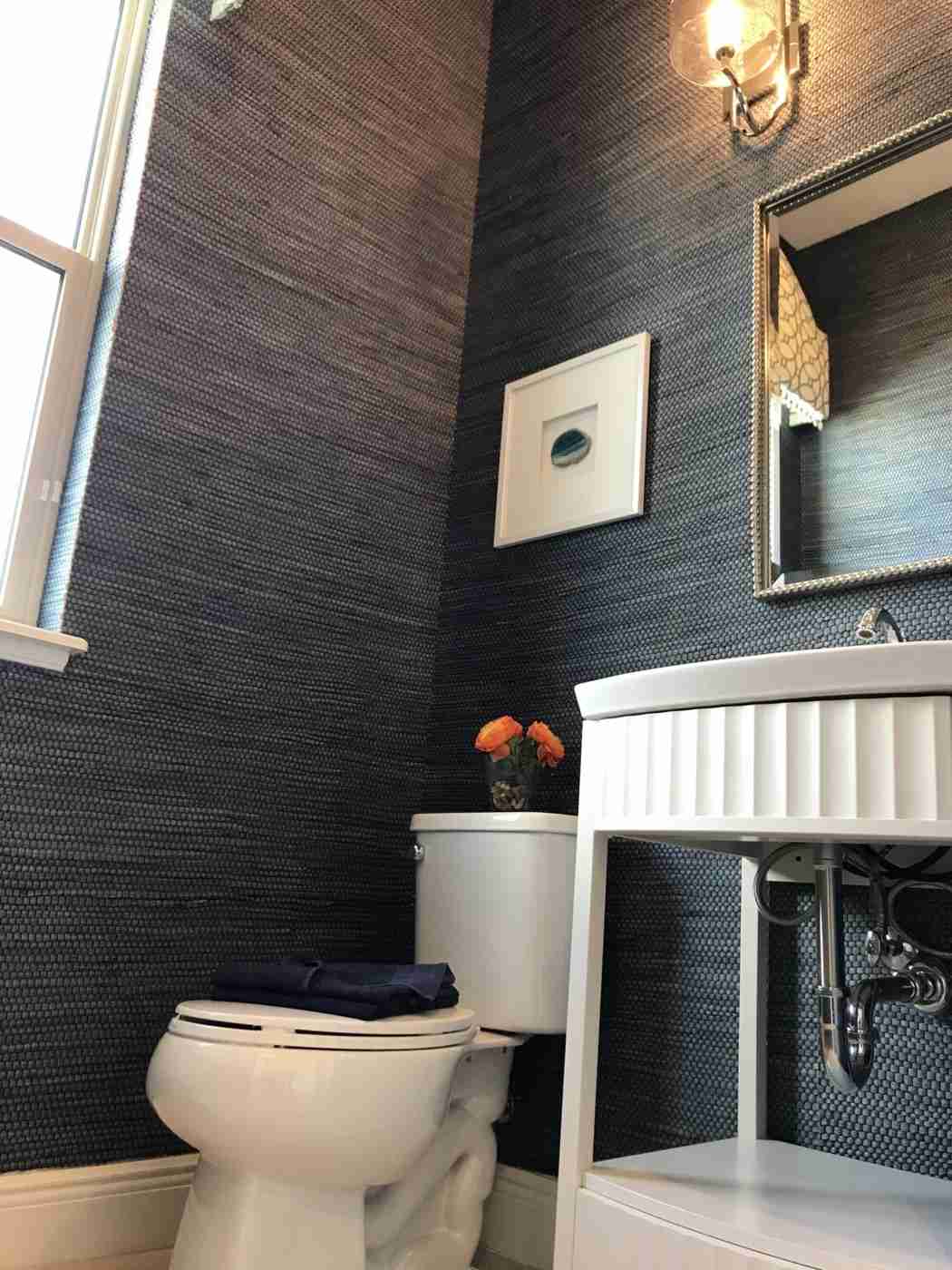 Luxury bathroom featuring dark textured grasscloth wallpaper dark wood vanity warm ambient backlight.