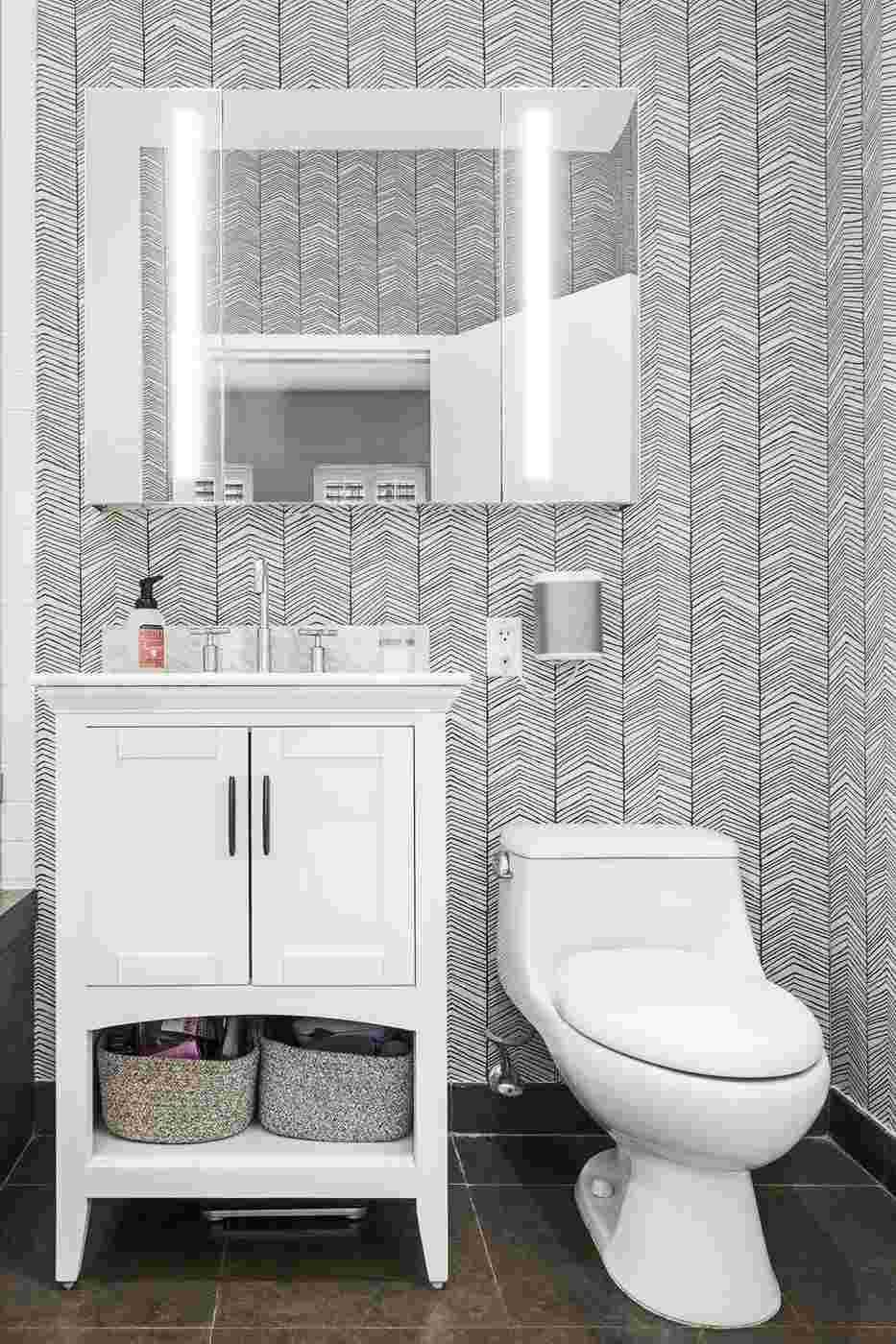 Modern bathroom with soft gray chevron wallpaper white vanity mirror sleek sconce light.