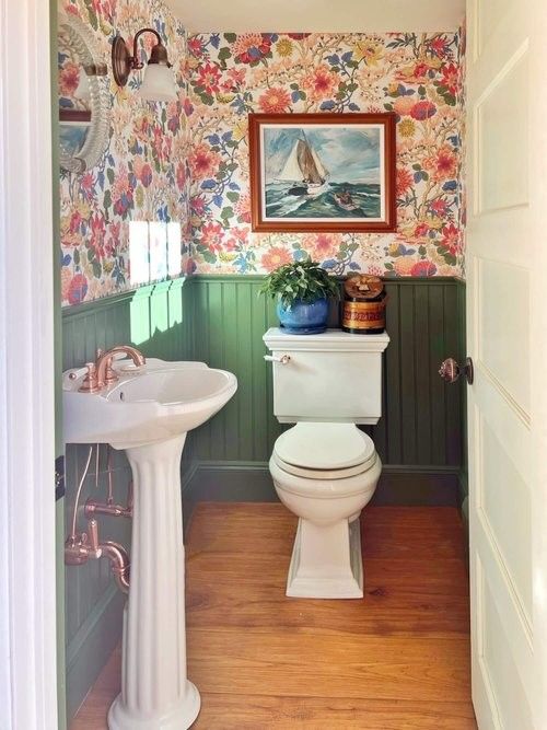 Green palm wallpaper paired with a bold orange door in a eclectic bathroom.