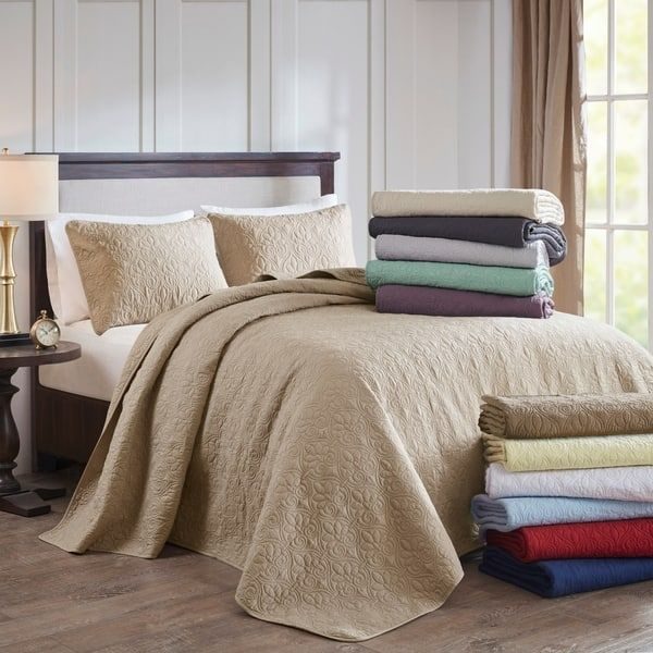 Peaceful bedroom with sage green comforter set, plush white pillows, natural rattan accent chair, gentle natural light