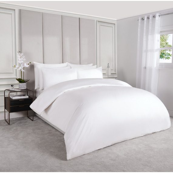 Coastal bedroom with light rattan bed frame, white linen duvet, blue striped pillows, warm sunlight.