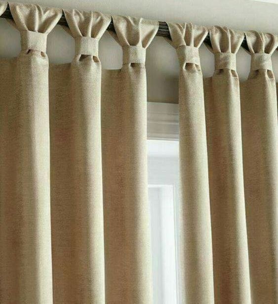 Extra long cream curtains covering an entire wall in a spacious bedroom with a king bed.