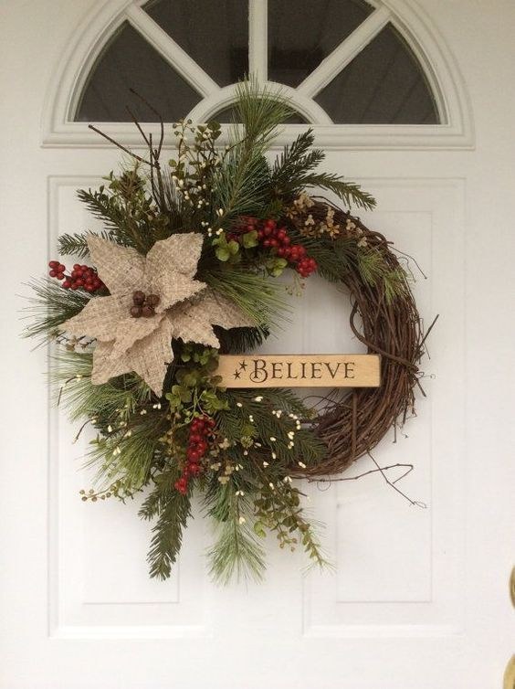 Rustic wooden porch door featuring a believe sign wreath with natural twig base and warm light.