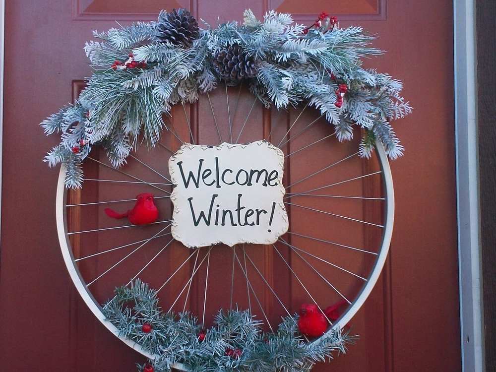 Vintage metal bicycle wheel wreath decorated with pine needles and red berries on a covered porch.