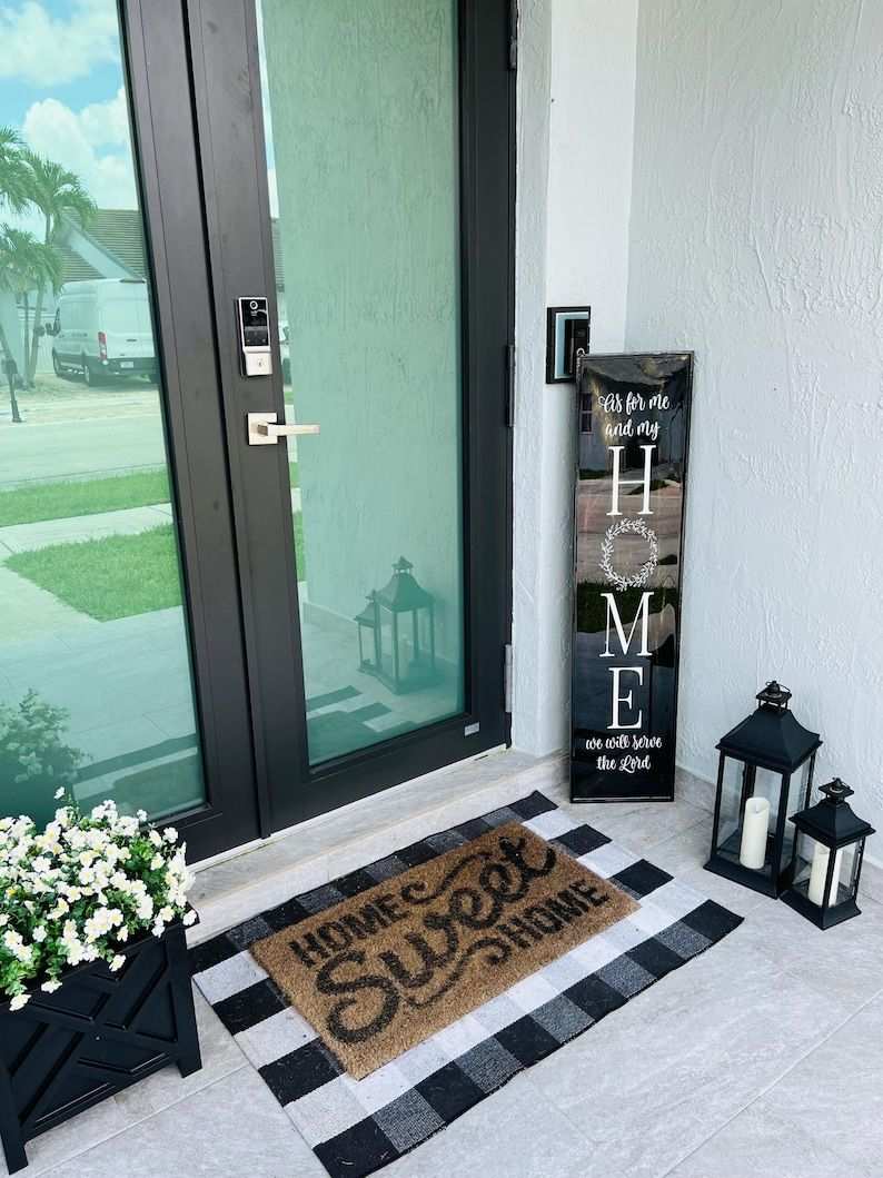 Front porch entry with black wooden welcome sign, wicker chair, and amber string lights