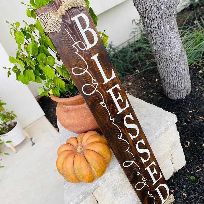 Front porch with a vertical dark wood sign, orange pumpkin, wicker bench, soft dusk lighting.