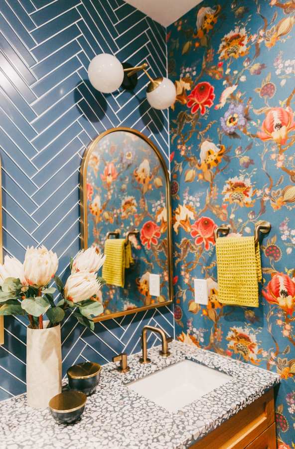 Navy blue floral wallpaper highlighted by a tall brushed brass arched mirror and vintage sconces