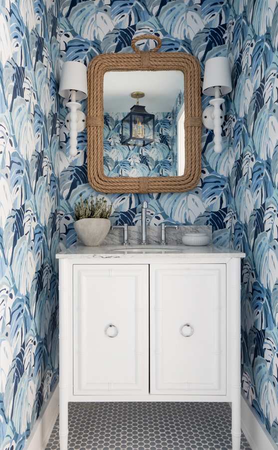 Dusty blue palm leaf wallpaper paired with a mid-century wood vanity and round illuminated mirror