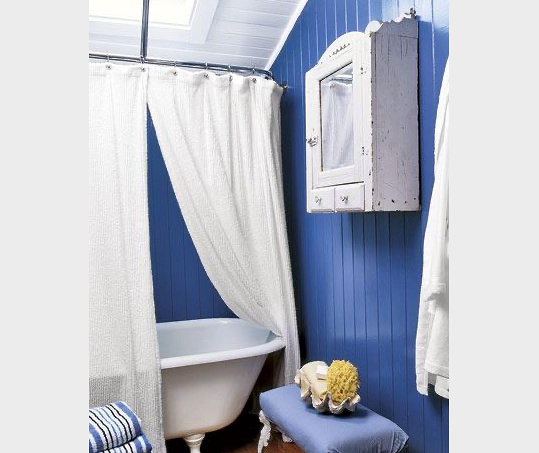 Moody royal blue wainscoting paneled walls framing a white clawfoot tub with floor standing brass faucet