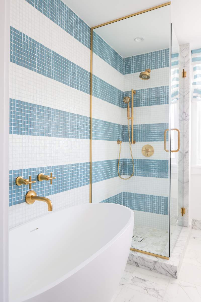 Blue and white vertical striped tile shower wall accented with brushed gold rainfall showerhead