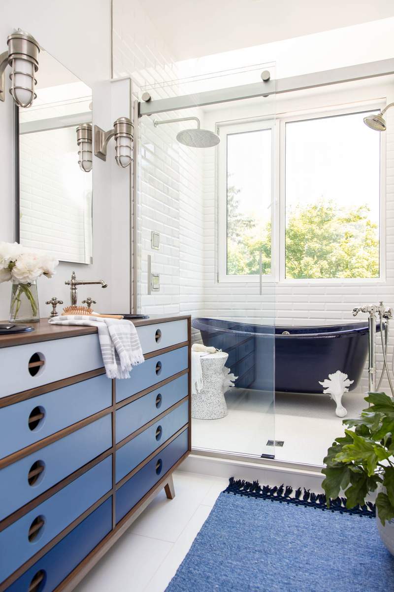 Midnight blue vanity cabinet next to a seamless frameless glass shower enclosure with brass fixtures