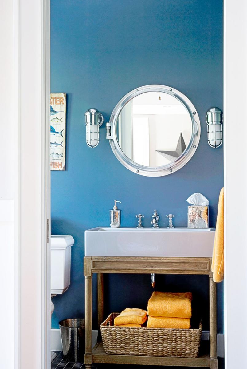 Deep slate blue painted bathroom walls featuring a large round brass mirror over a slim console sink