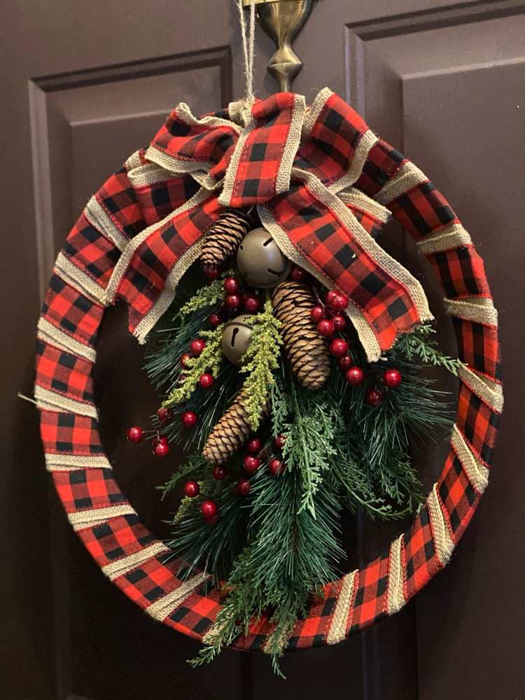 Classic porch front door adorned with buffalo plaid ribbon, pinecones, and jingle bells under porch lighting.