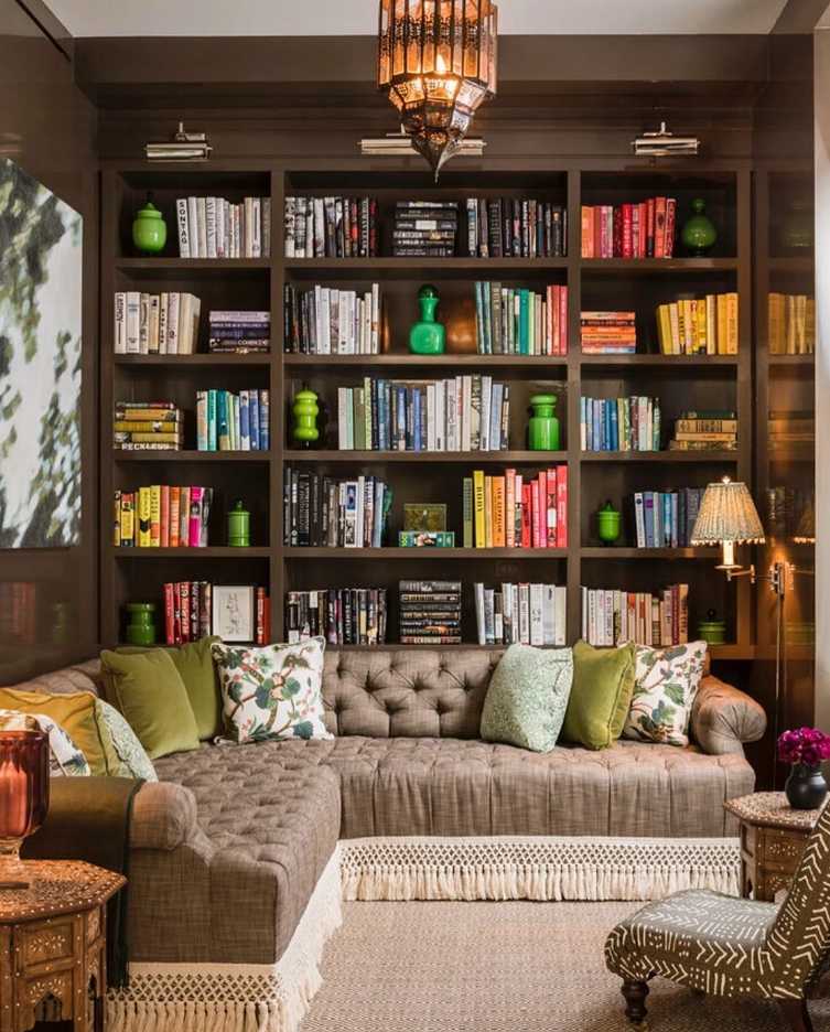 Sectional sofa in soft gray, integrated walnut bookshelf, floor‑to‑ceiling windows, ambient ceiling lights.