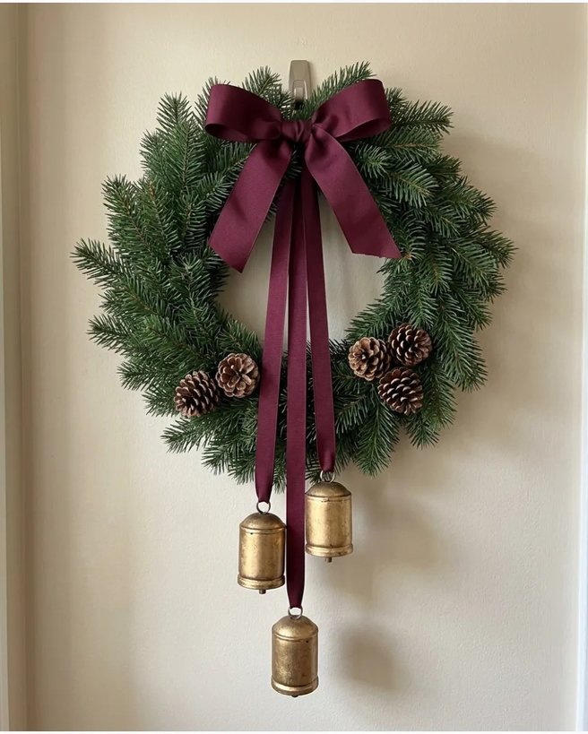Burgundy bow gold bells wreath on dark door with warm light