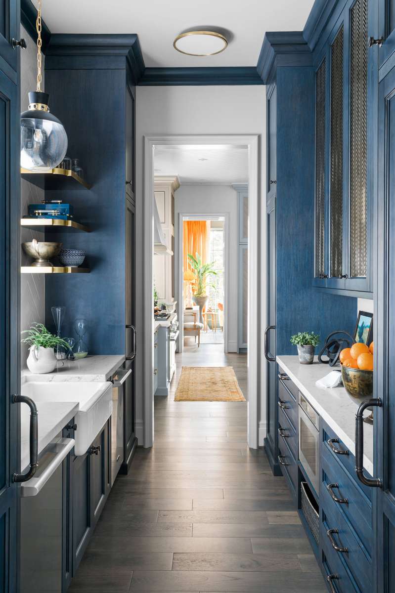 A narrow butler’s pantry in a calming blue hue with galley-style cabinets and integrated appliances.