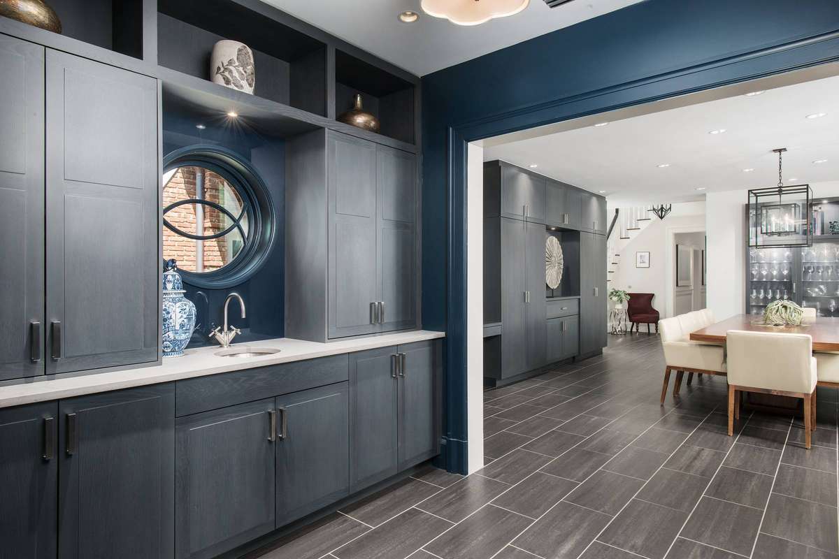 A blue-themed butler’s pantry featuring a unique round window and symmetrical open shelving.