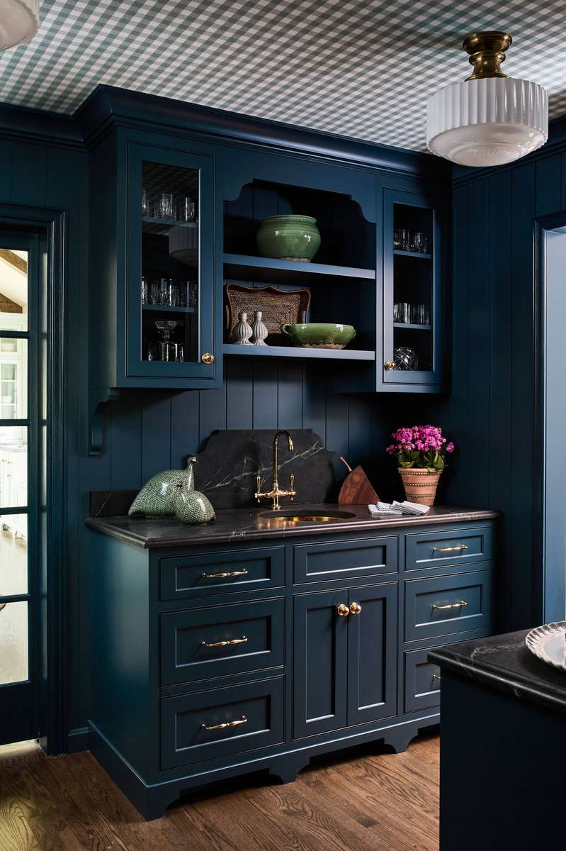 A navy blue butler’s pantry with white beadboard walls and brass lighting fixtures.
