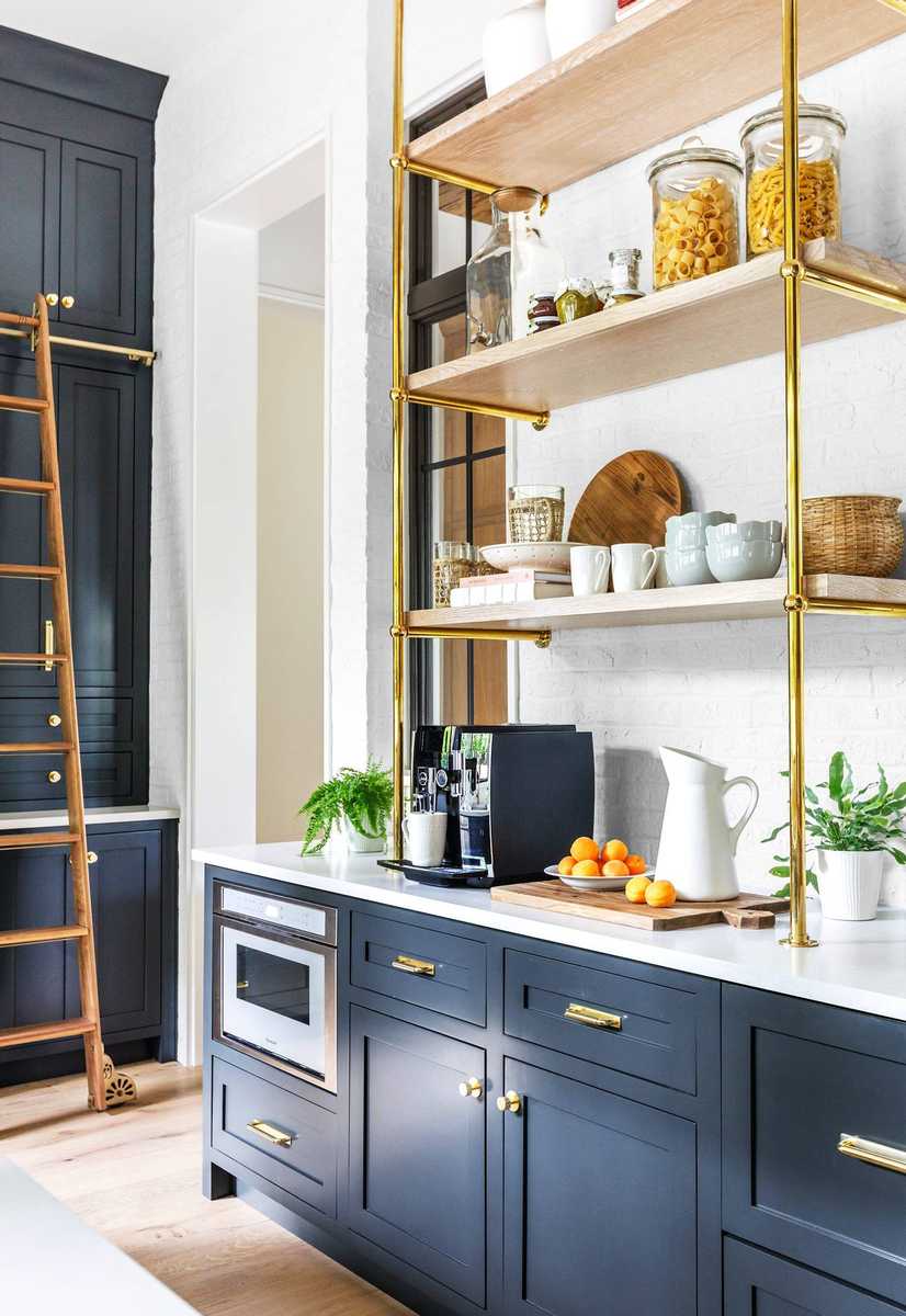 A luxury butler’s pantry with dark navy cabinets and open brass floating shelves.
