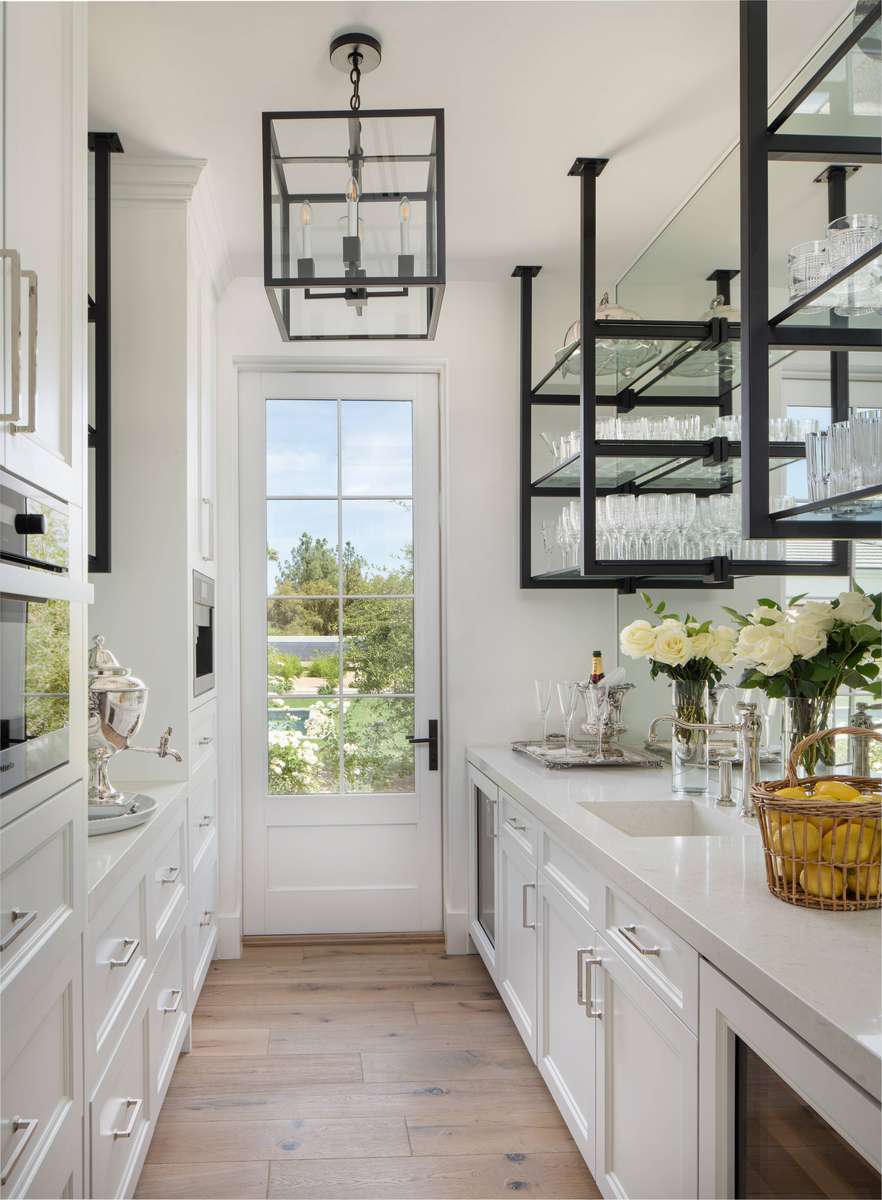 Efficient white galley butler's pantry featuring continuous marble countertops and flush cabinet storage.
