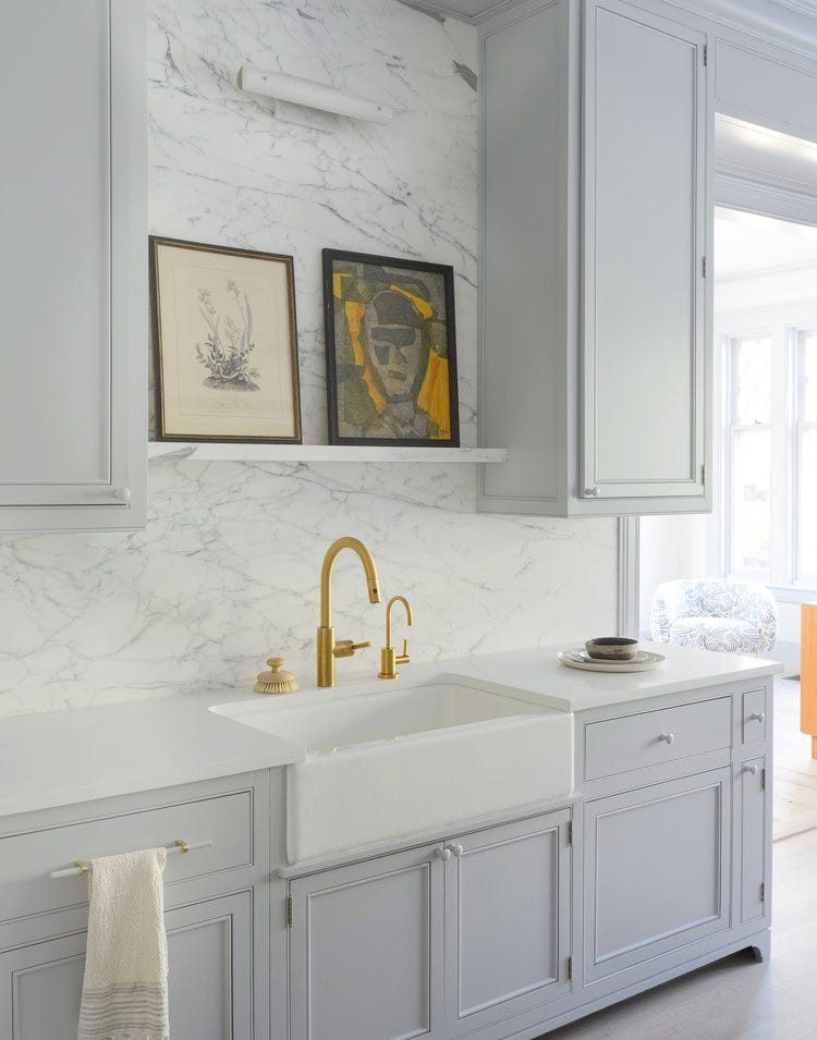 Luxurious white butler's pantry featuring a full slab marble backsplash and unlacquered brass hardware.