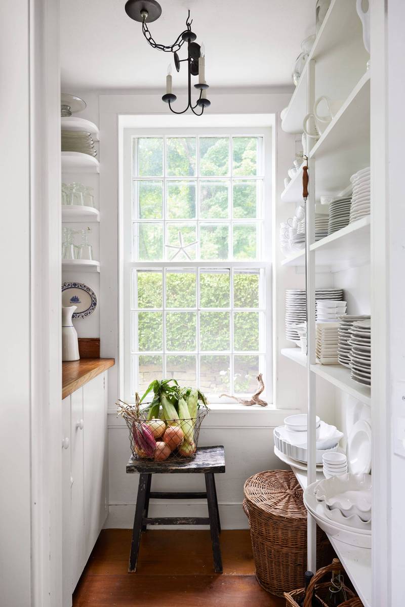 Sunlit white butler's pantry with a large window framing garden views above marble counters.