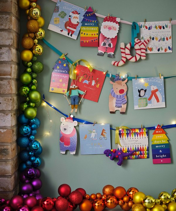 Modern hallway displaying vertical earthy-toned velvet ribbons pinned with holiday cards under sconce light.