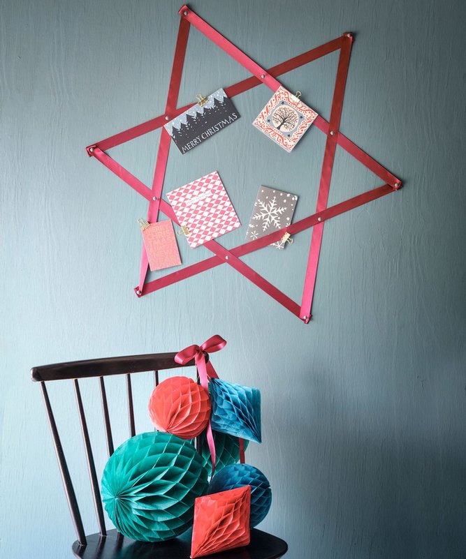 Cozy bedroom wall displaying large geometric wooden star silhouette holding cards with fairy lights.