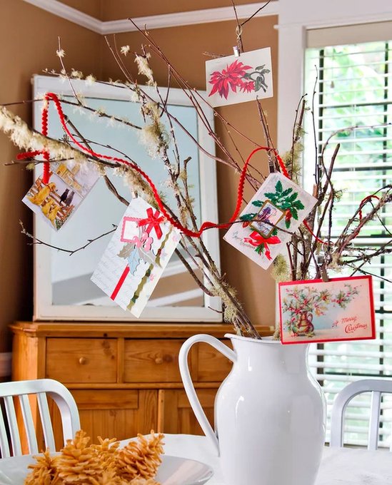 Cozy entryway table featuring black wrought iron spiral tree holding seasonal cards beside candles.