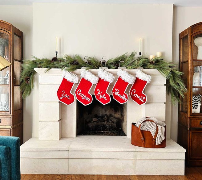 Symmetrical living room stone mantel styled with tailored cedar garland, antique mirror, and warm illumination.