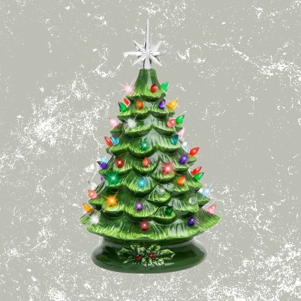 Small ceramic lit christmas tree with a frosted finish sitting on a marble coffee table with soft ambient light.