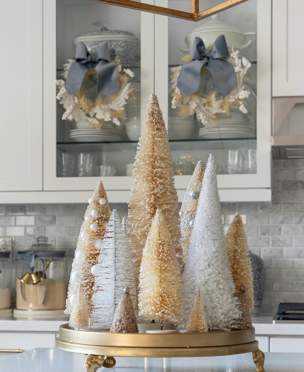 Group of champagne gold bottle brush trees on a sideboard with lights.
