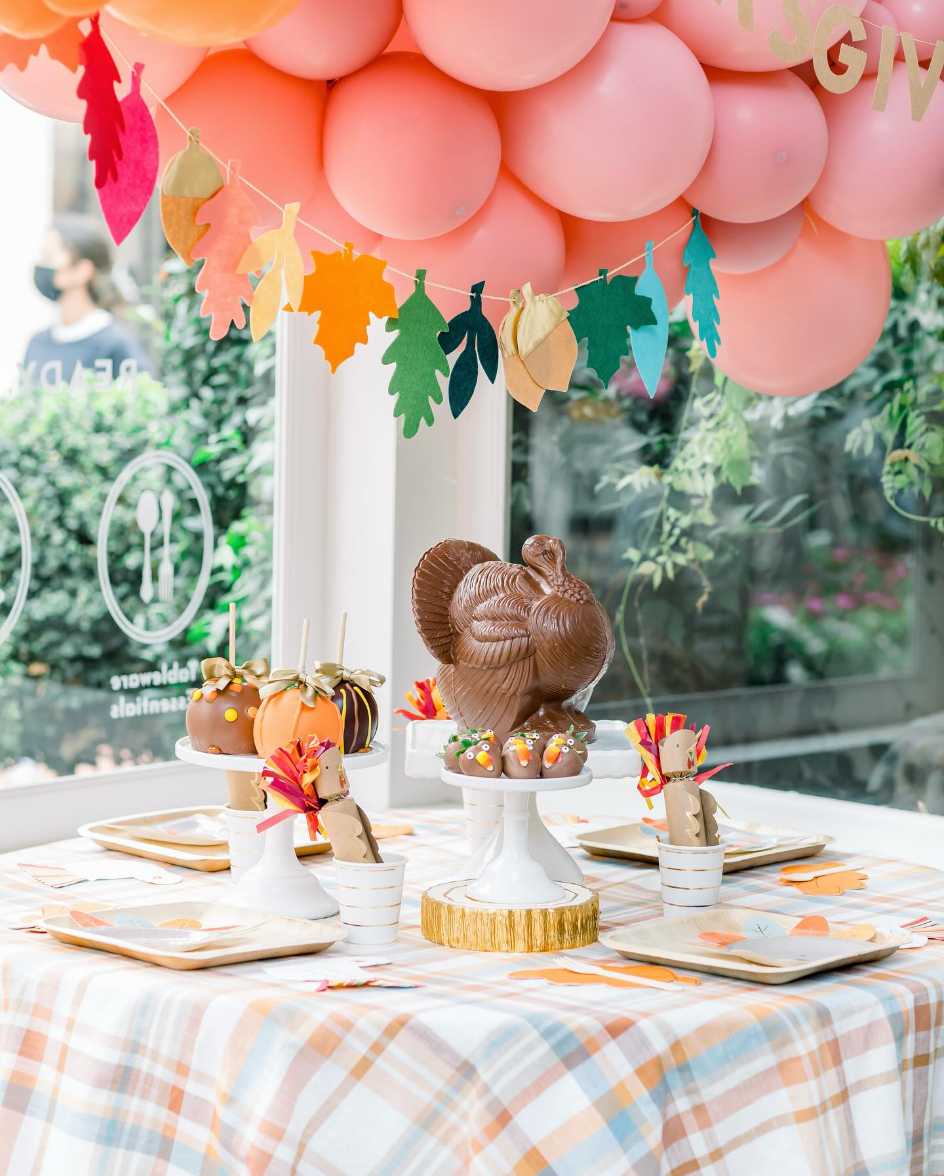 Dessert table featuring chocolate turkey sculptures, dark ganache, gold accents, soft pastel backdrop, ambient lighting