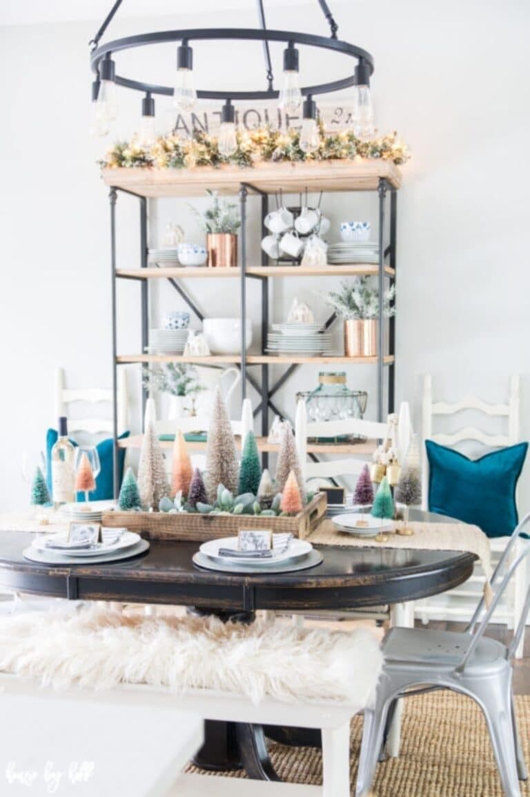 Dining room table set with festive greenery, gold cutlery, white linen tablecloth, warm candles.
