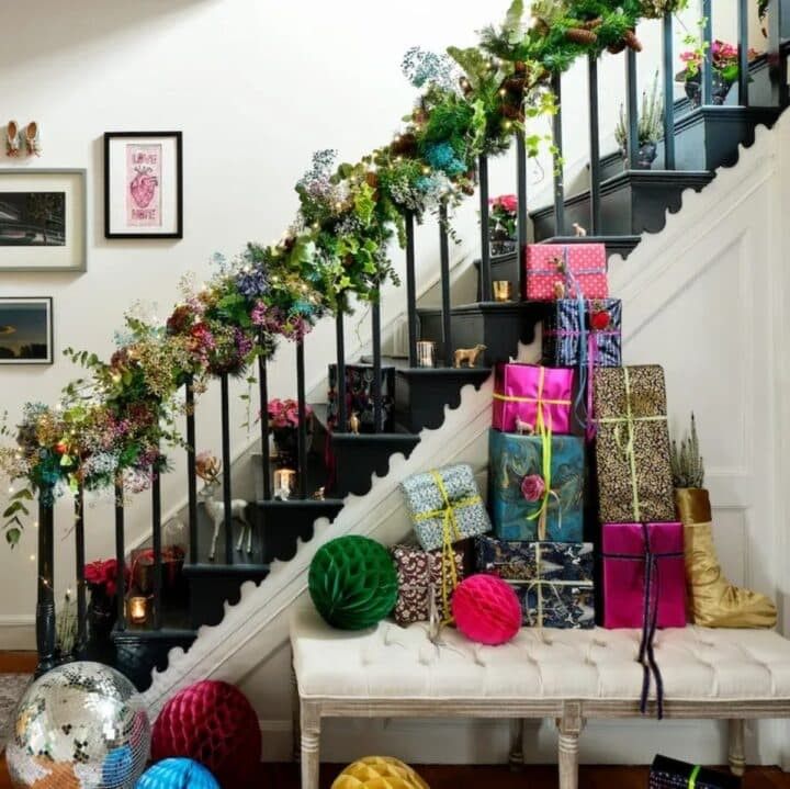 A staircase railing adorned with thick green garland, ribbons, and twinkling fairy lights.