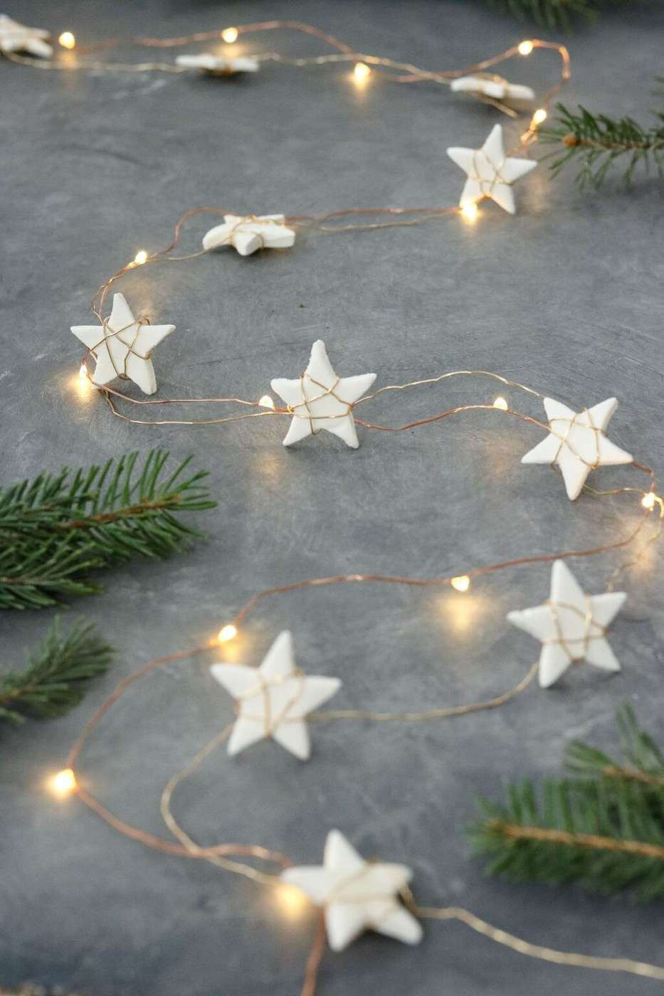 Delicate fairy lights with small star-shaped covers hanging against a dark bedroom wall.