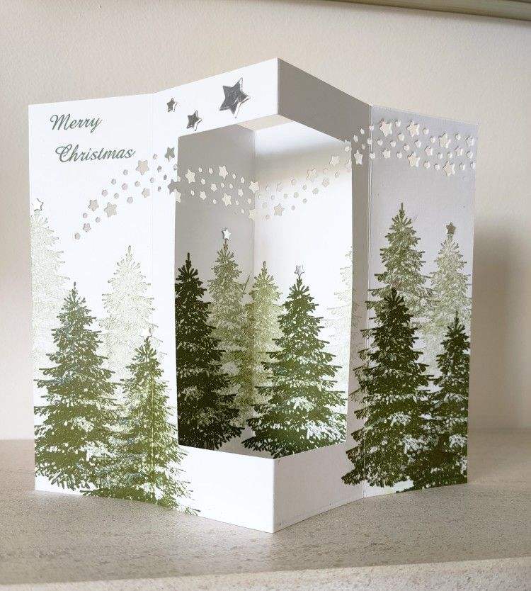 A large eucalyptus wreath adorned with brass clips displaying colorful hand-painted Christmas cards.
