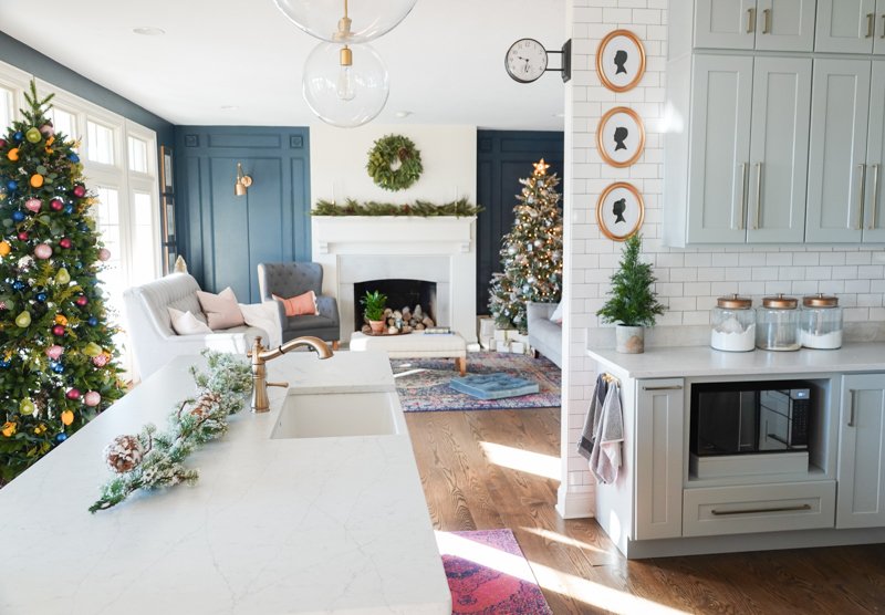 A front porch decorated with lanterns, a large wreath, and potted mini trees.