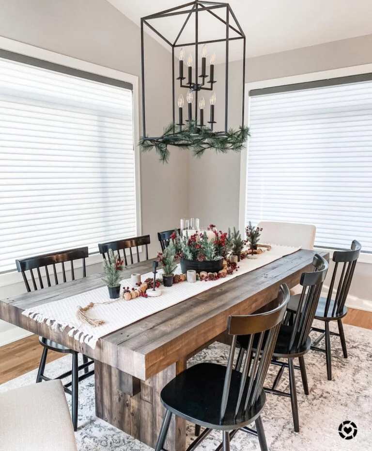 Dining table with pinecone garland and a black iron chandelier overhead.